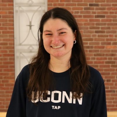 Emily Leahy in a UConn Shirt in front of a brick wall
