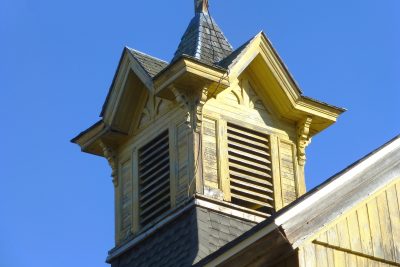Yellow wooden cupola with louvered vents and decorative trim against a clear blue sky
