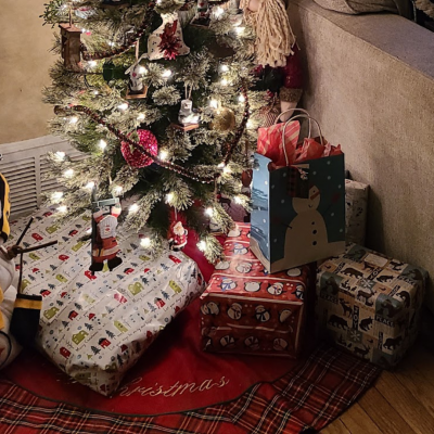A decorated Christmas tree with white lights and various ornaments, surrounded by wrapped presents on a red tree skirt.