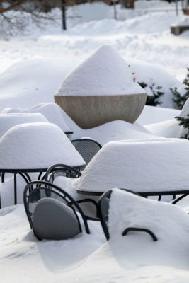 Outdoor metal tables and chairs covered in deep snow, with large mounds of snow piled on top and around them in a winter landscape.