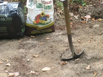 Shovel digging into dirt with one white and one black bag of soil in the background.