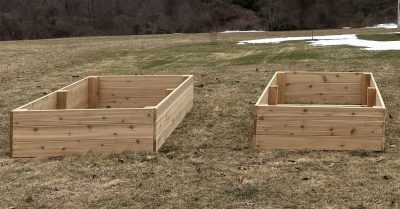 Two empty wooden raised garden beds placed on a grassy field, spaced apart and framed with light-colored lumber.